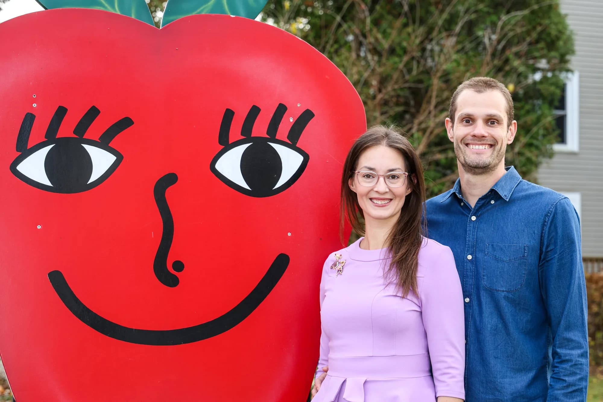 Nate and Laurie Dillman standing beside the orchard's smiling apple sign